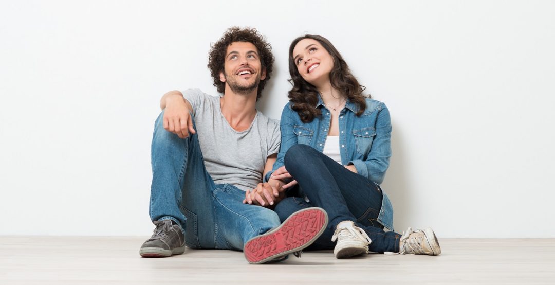 Portrait Of Happy Young Couple Sitting On Floor Looking Up Ready for your text or product